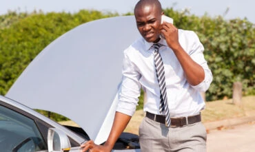 man on phone with roadside assistance in front of broken down car