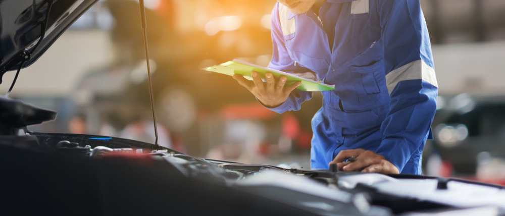 mechanic working on car with hood up and check list