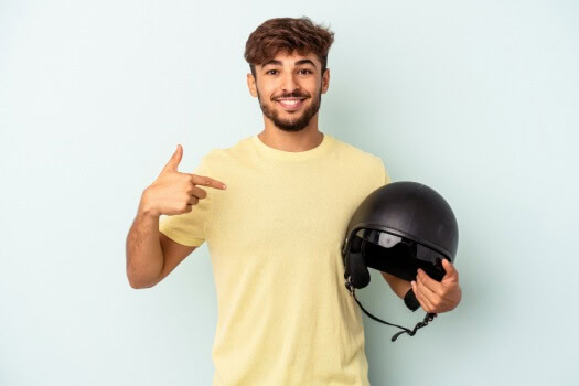 Man with yellow shirt pointing to motorcycle helmet in his arms and smiling - cheap motorcycle insurance in Georgia.