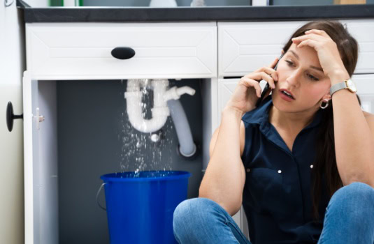 Woman sitting on the floor, worried about water leak in her sink and calling for help - Affordable Renters Insurance in Georgia 